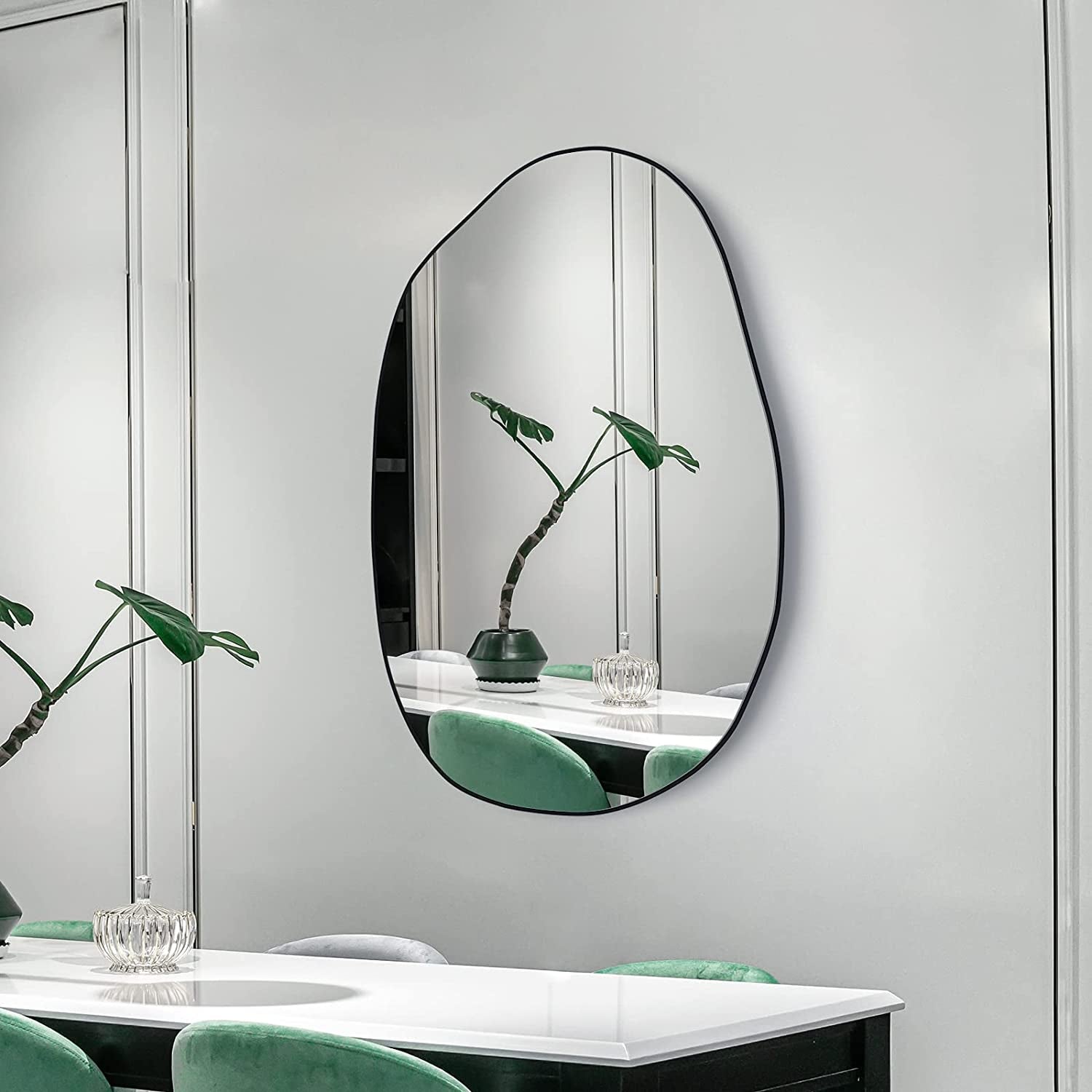 Modern irregular oval wall mirror with black frame for dining room or living space decor.

