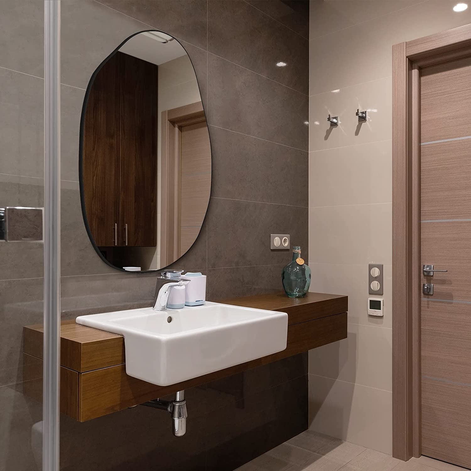 Irregular oval wall mirror with black frame, ideal for modern bathroom vanity decor.
