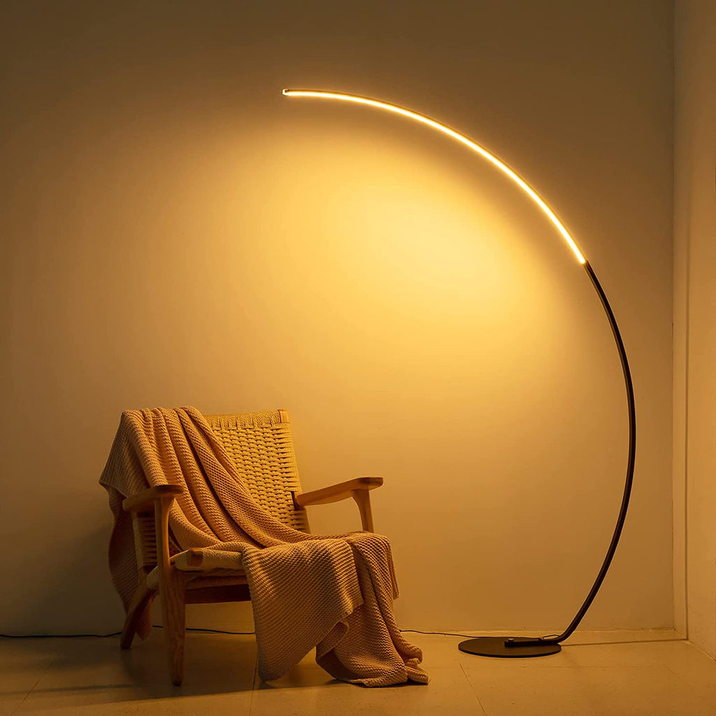 Modern arc floor lamp with warm LED lighting beside chair