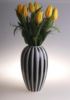 Modern black and white striped ceramic vase with yellow tulips for stylish decor.
