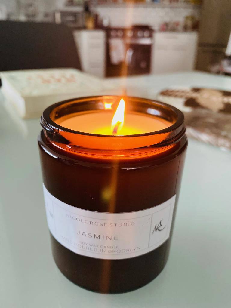 Jasmine scented soy candle burning in amber glass jar, relaxing aroma.

