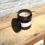 Lavender white sage soy candle in amber jar with dried herbs on top.
