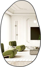 Irregular black-framed wall mirror reflecting modern living room with green chairs.
