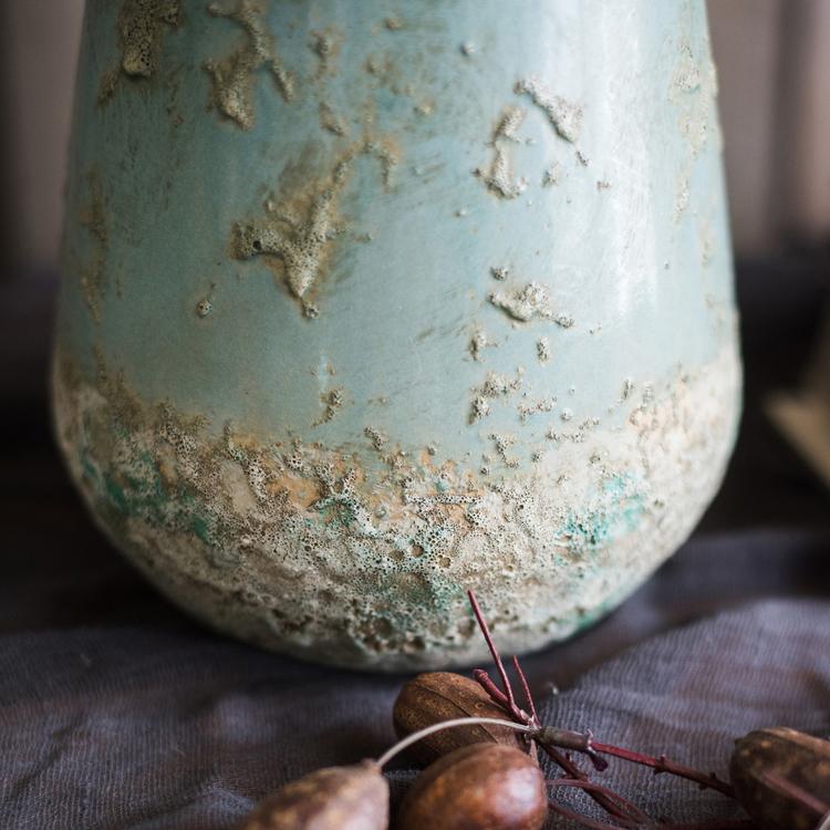 Close-up of rustic green ceramic vase with distressed textured finish for vintage decor.
