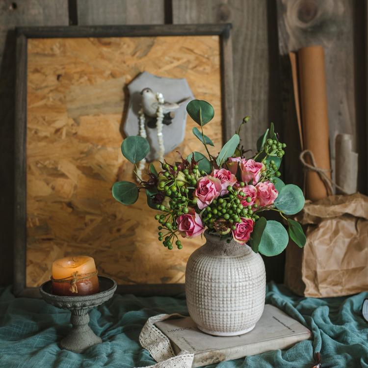 Rustic ceramic vase with pink roses and greenery for farmhouse-style home decor.
